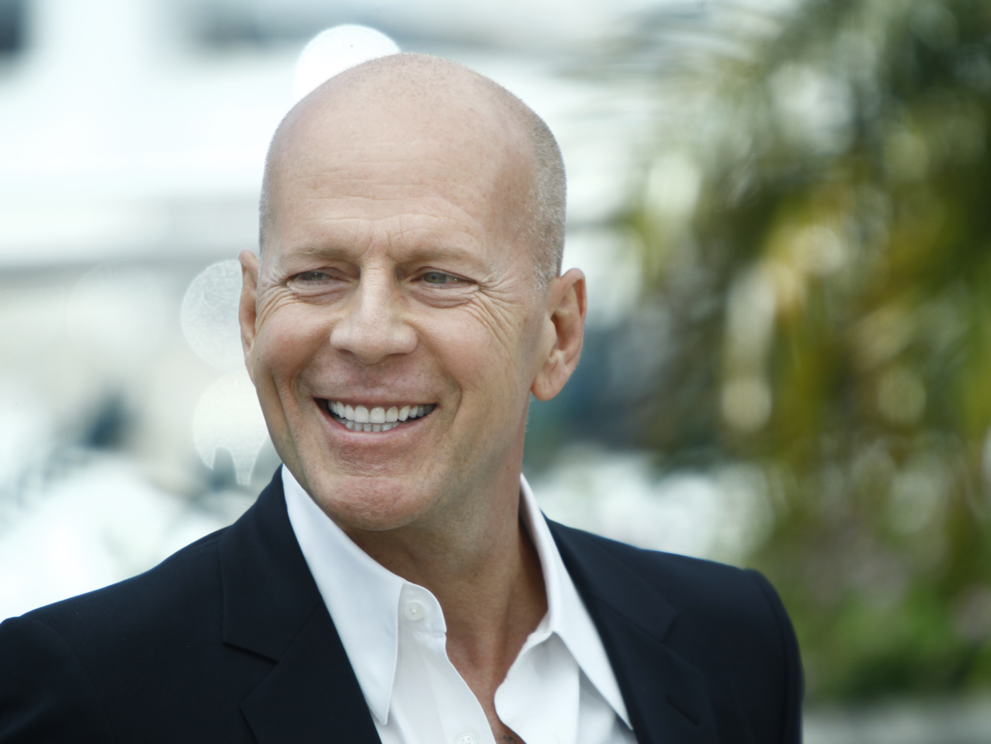 Bruce Willis smiling in a chic black suit with a white shirt