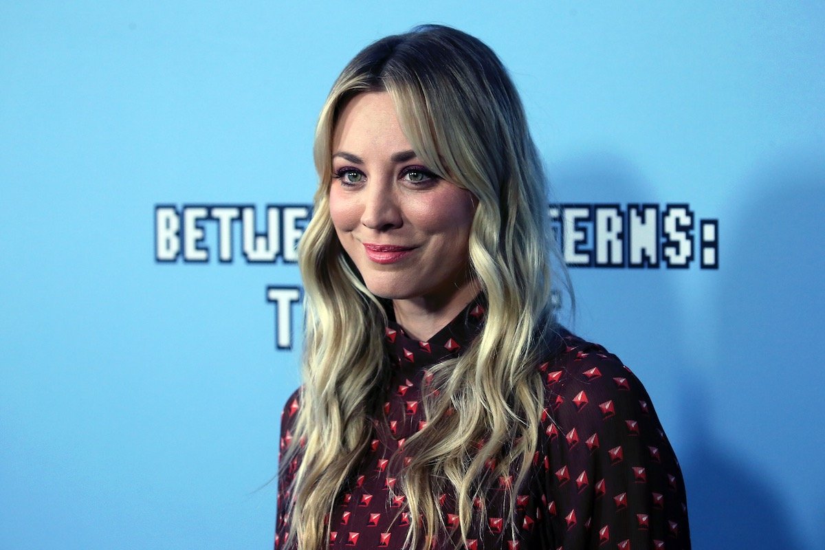 Kaley Cuoco in a red and black patterned dress against a blue background