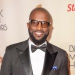 Rickey Smiley at the BLACK MUSIC HONORS wearing a black tux, blue pocket square, and glasses.