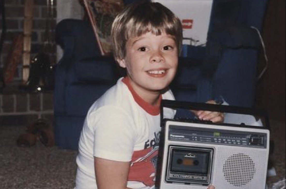 Ryan Seacrest as a child, smiling at the camera while holding up a radio
