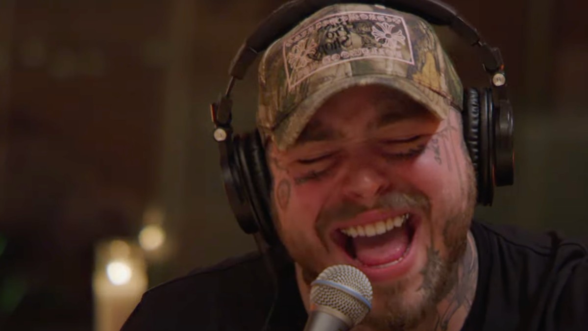Post Malone, wearing a camo patterned hat, sings country