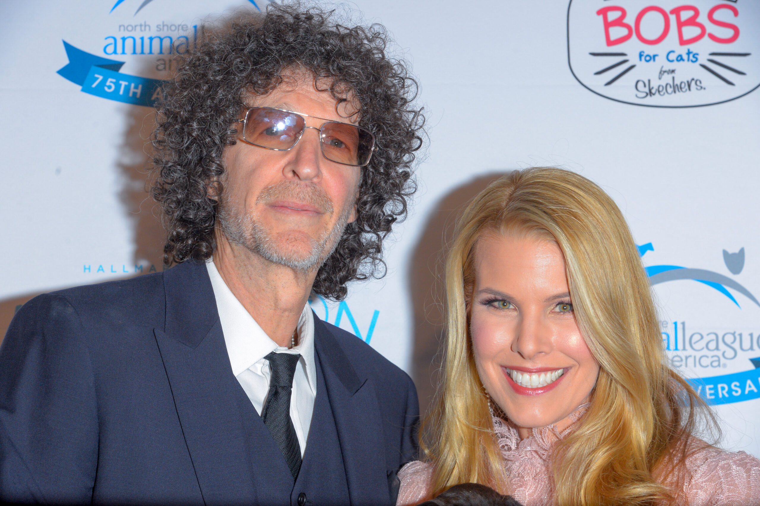 Howard Stern wears a black suit and tie and stands with Beth Stern