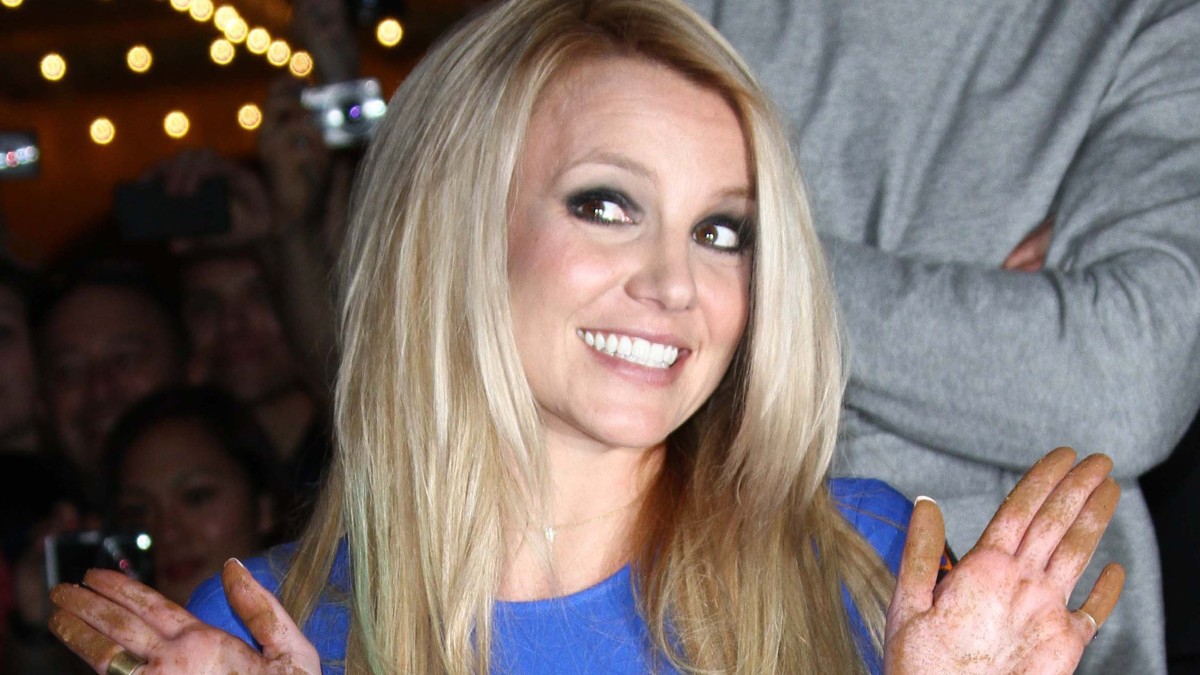 Britney Spears wears a blue dress and holds up her hands