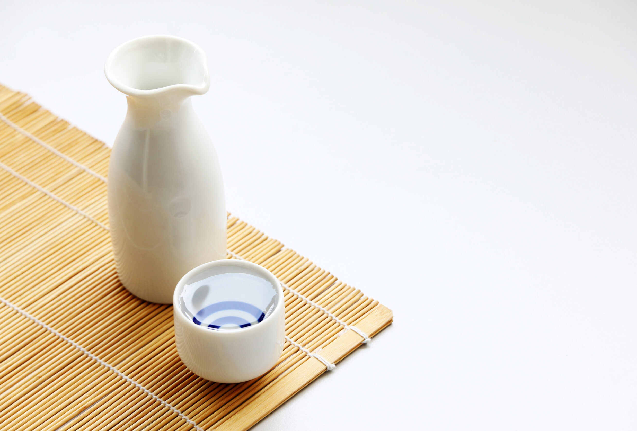 Sake in a traditional serving glass and bottle on a bamboo mat.