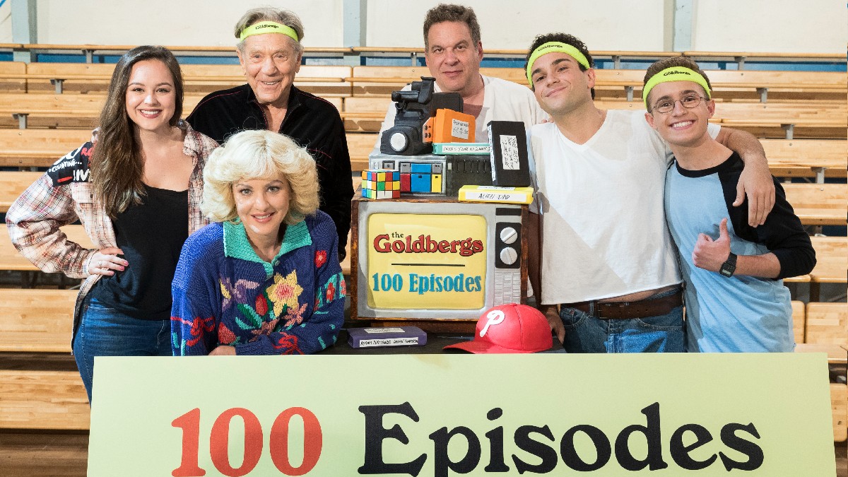 Several cast members from The Goldbergs pose together behind a sign