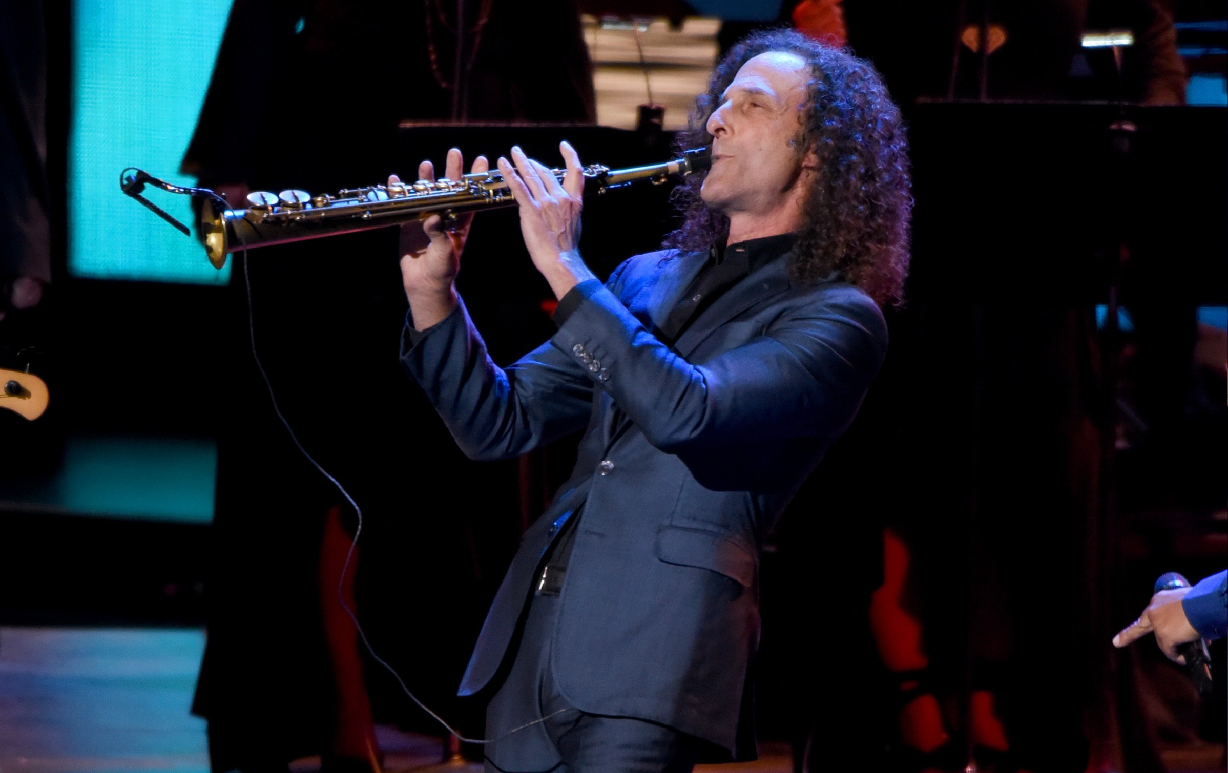Kenny G wears a dark suit as he plays the saxophone onstage