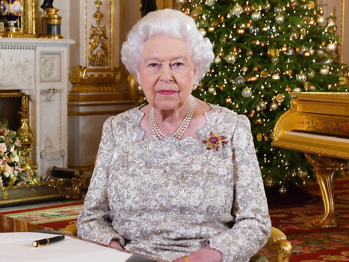 Queen Elizabeth sits in chair in front of Christmas tree
