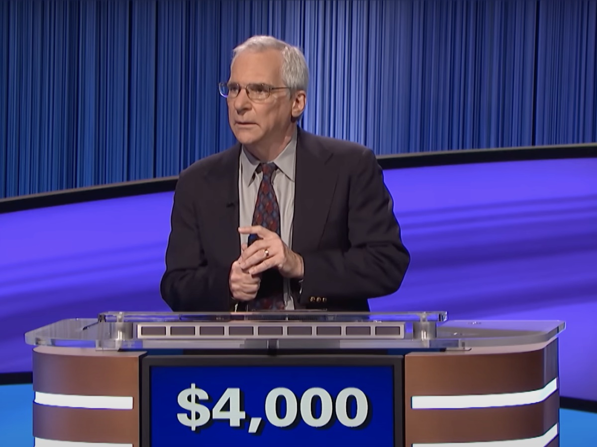 screenshot of Sam Buttrey on Jeopardy! holding his buzzer in his right hand while holding his left index finger above it